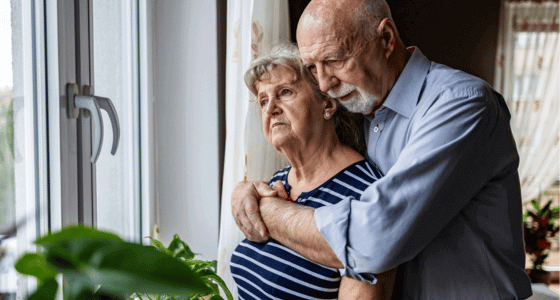 Man and woman looking pensive looking out of window at home