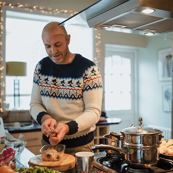 Man peeling vegetables in kitchen wearing a Christmas jumper