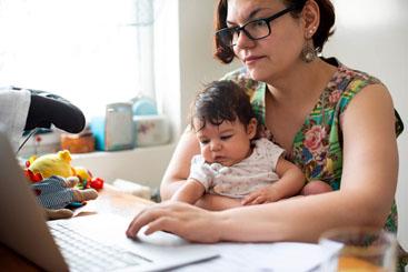 Woman holding a baby whilst looking on a laptop