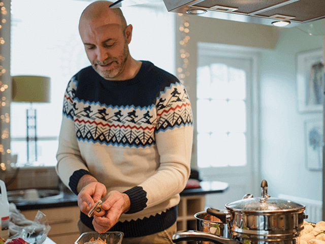Man peeling vegetables in kitchen wearing a Christmas jumper